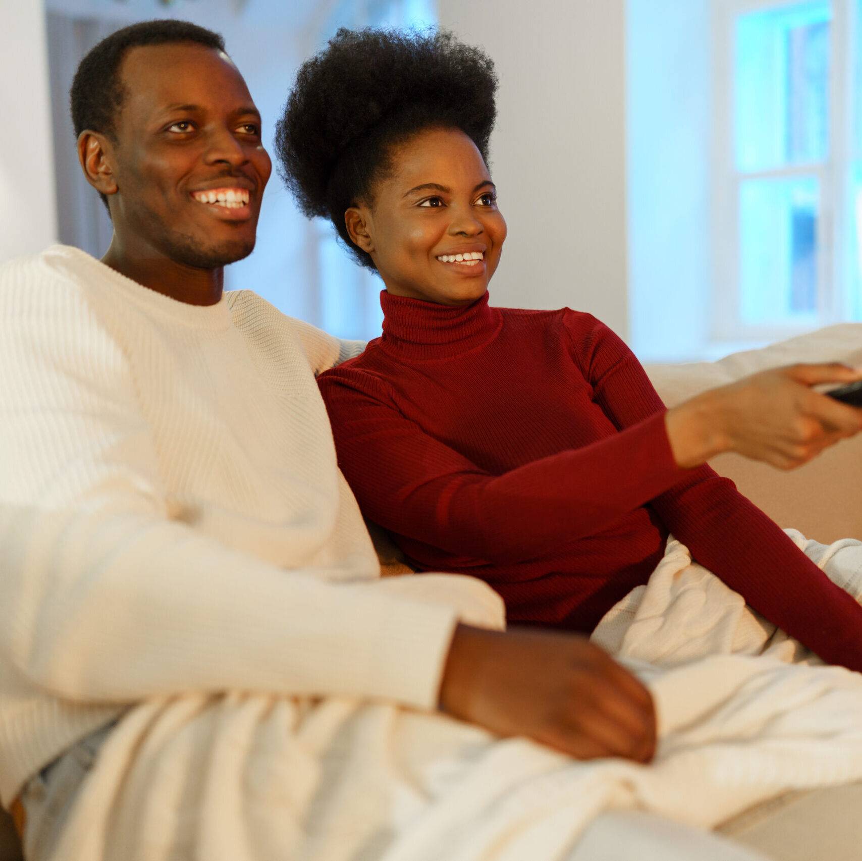 Young happy afro american family couple man and woman watch comedy show on tv and laughing