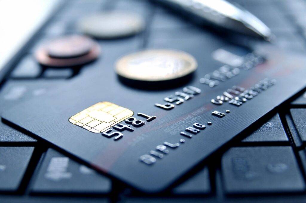 Close-up image of a black credit card on a black keyboard with a real penny resting on the card, emphasizing financial concepts.
